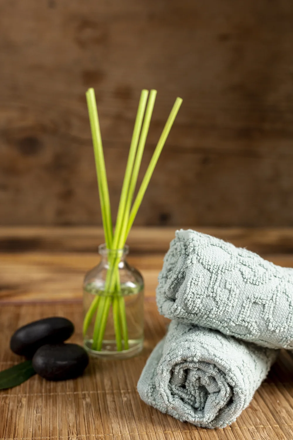 Soft spa towels, smooth massage stones, and green stems in a glass vase